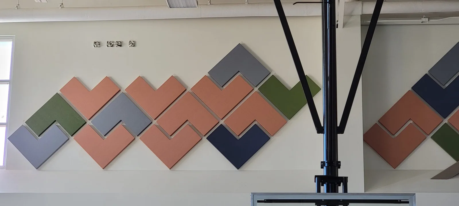 Color-block acoustic wall panels installed high across a gymnasium wall