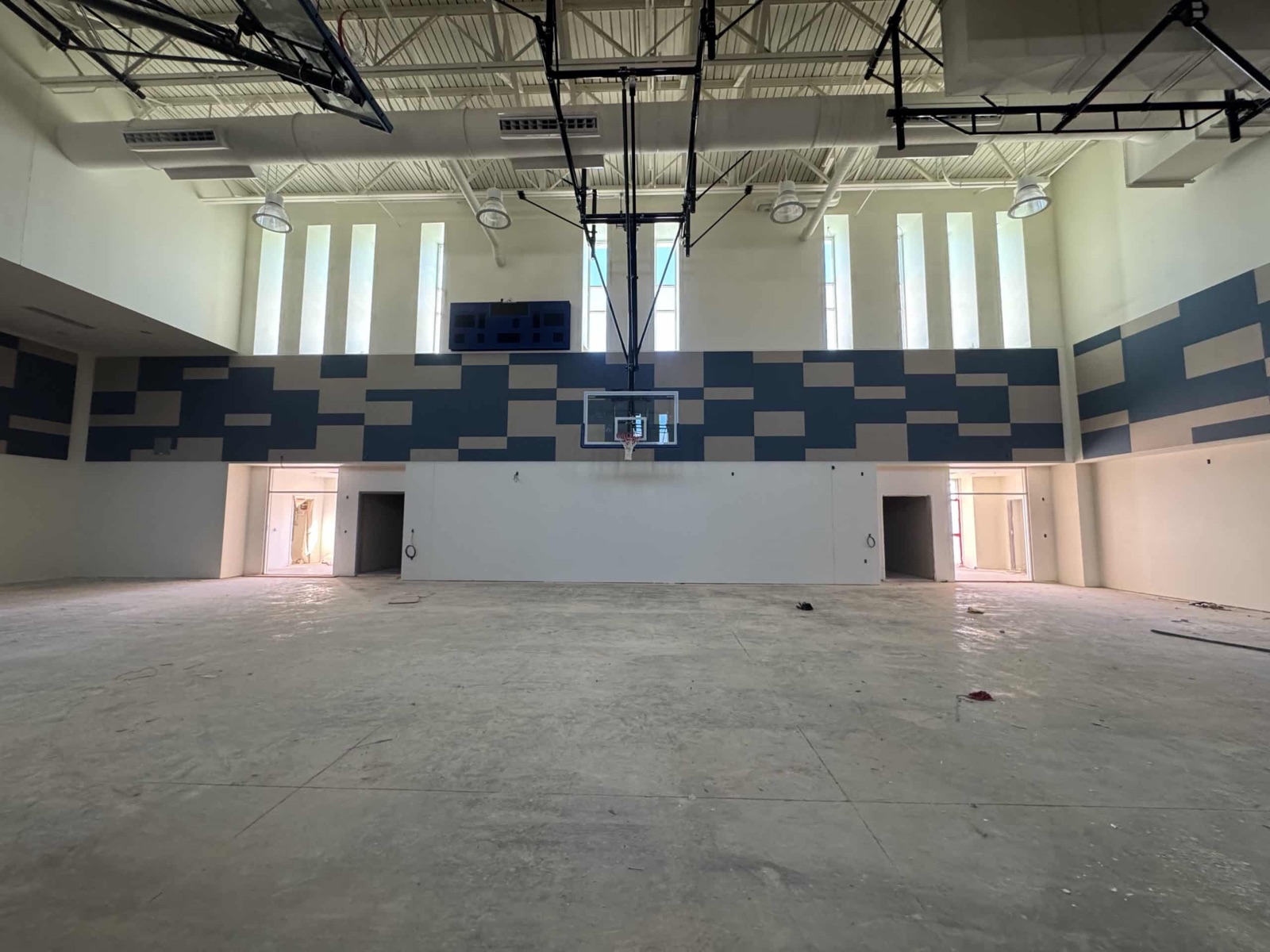 Wide gymnasium during construction with blue and gray upper-wall acoustic panels