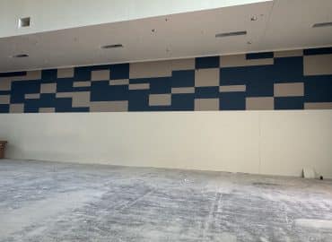 Blue and gray rectangular acoustic panels across an unfinished multipurpose-room wall.