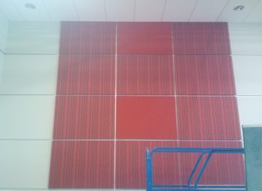 Tall red segmented acoustic wall panel above construction equipment.