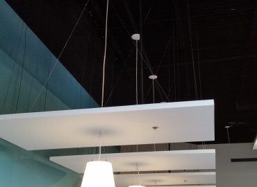 Suspended white rectangular acoustic clouds below tall teal walls.