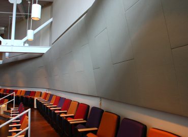 Large gray wall panels running along bright auditorium seating.