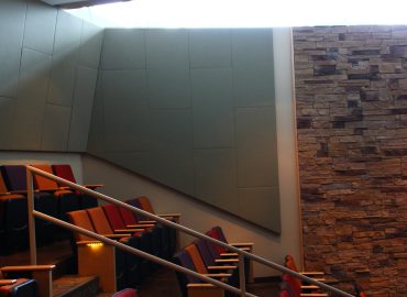Tall gray wall panels beside a stone column in an auditorium.